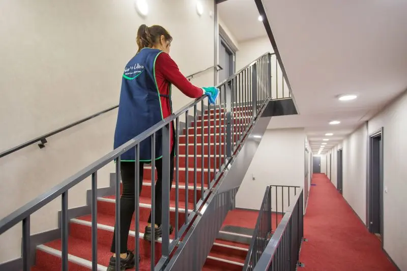 Employée d'entretien Nett' Ultra désinfectant la rampe d'un escalier.