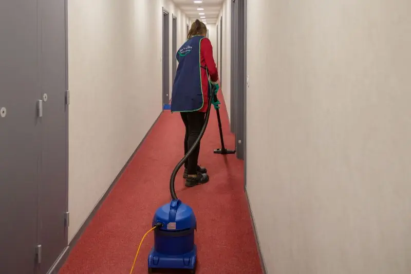agent d'entretien passe l'aspirateur dans un couloir