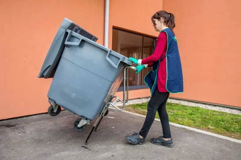 agent d'entretien nettoie une poubelle extérieure