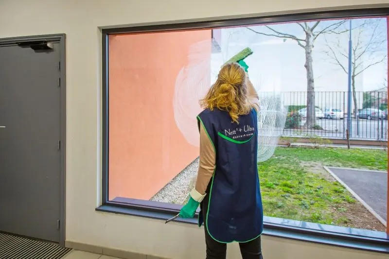 agent d'entretien nettoie une vitre dans un hall d'entrée